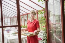 Portrait of woman in conservatory holding wooden tray — Stock Photo