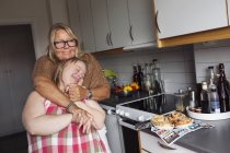Мати обіймає дочку з синдромом Дауна на кухні — стокове фото