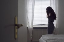 Замислений молода жінка стоїть вікно — стокове фото