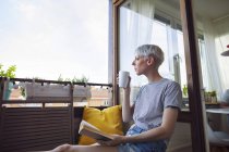 Donna che legge libro sul balcone e beve caffè — Foto stock