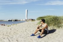 Junger Mann sitzt am Strand — Stockfoto