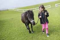 Chica (4-5) caminando con pony en la granja - foto de stock