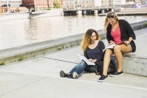Two young women reading books by river — Stock Photo