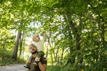 Padre che porta il figlio (2-3) sulle spalle sotto gli alberi — Foto stock
