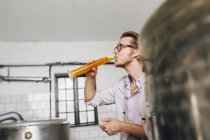 Brewery worker drinking beer from beaker — Stock Photo