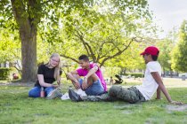 Ragazza adolescente e ragazzi adolescenti (14-15) seduti nel parco — Foto stock