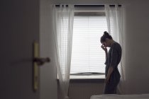 Nachdenkliche junge Frau steht am Fenster — Stockfoto