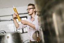 Trabajador cervecero examinando cerveza en vaso de precipitados - foto de stock