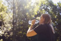 Жінка п'є воду в лісі вдень — стокове фото