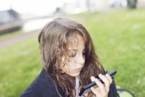 Дівчина (4-5) сидячи на траві і за допомогою смарт-телефон — стокове фото