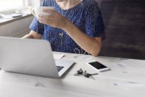 Жінка п'є каву і працює на ноутбуці — стокове фото