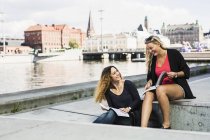 Two young women holding books by river — Stock Photo