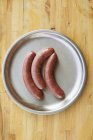 Studio shot of pork sausages on silver plate — Stock Photo