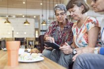 Three women using digital tablet in cafe — Stock Photo