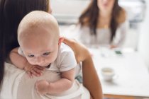 Mother holding baby son (2-5 months) and talking with friend in cafe — Stock Photo