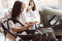 Two young women with baby stroller in cafe — Stock Photo