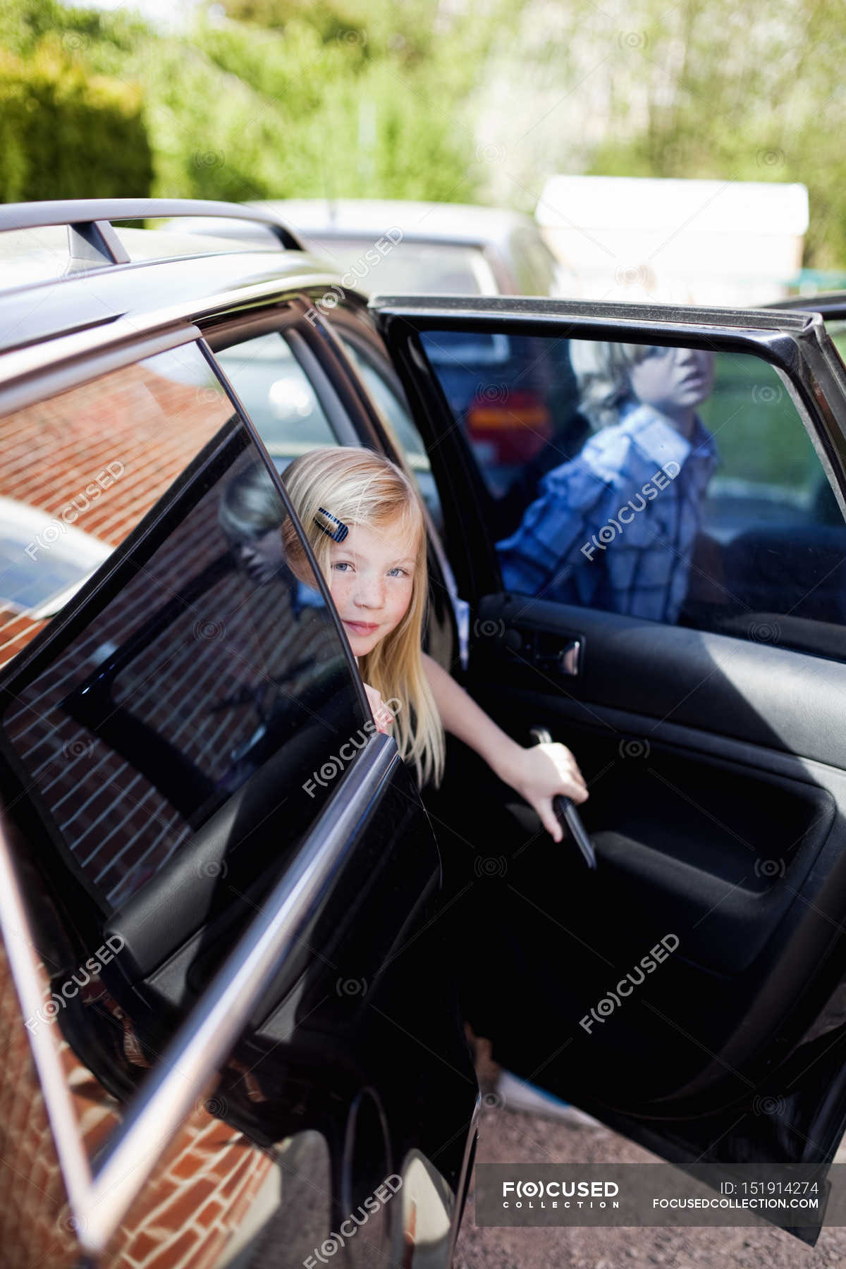 Girl Looking Through Open Door Of Car With Brother In Background