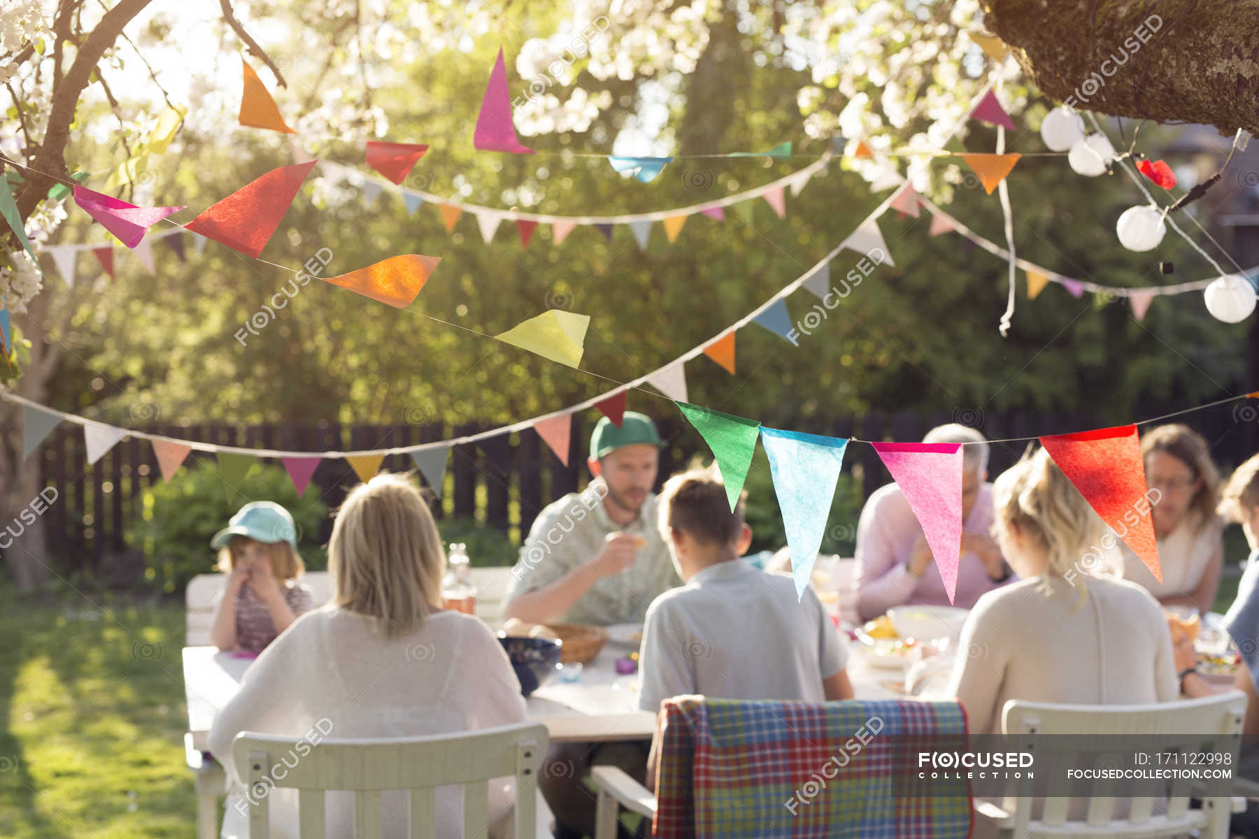 Family sitting at dinner table at garden party in back yard — boy ...