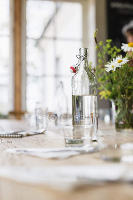 Garrafa de água de vidro por vaso de flor — Fotografia de Stock