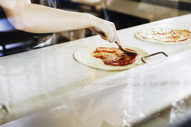 Mujer aplicando salsa sobre pizza - foto de stock