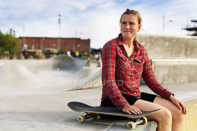 Жінка з скейтбордом сидить на рампі в скейт-парку — стокове фото