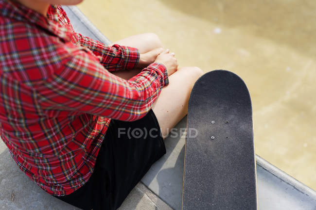 Женщина со скейтбордом сидит на рампе в скейт-парке — стоковое фото