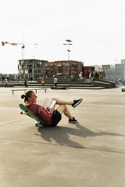 Mulher com livro inclinado no skate no parque — Fotografia de Stock