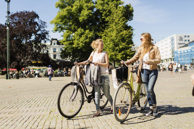 Amigos caminando con bicicletas en la ciudad - foto de stock