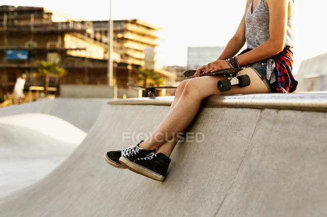 Teenage girl with skateboard sitting at edge — Stock Photo