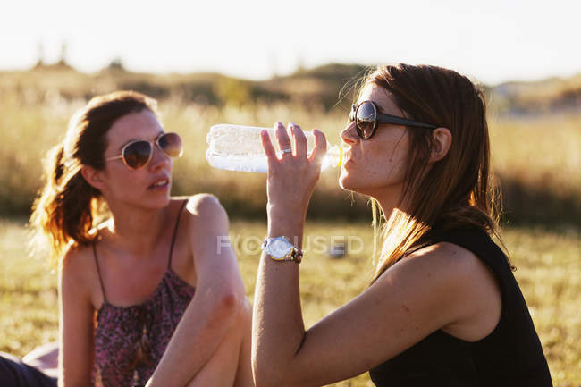 Mujer sentada junto a un amigo y bebiendo agua - foto de stock