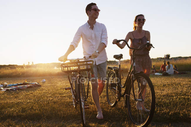 Amici a piedi con biciclette sul campo — Foto stock