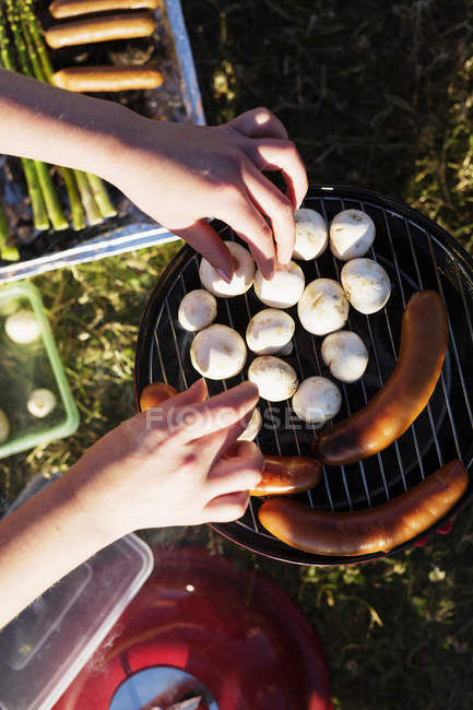 Mani che cucinano funghi e salsicce su barbecue — Foto stock