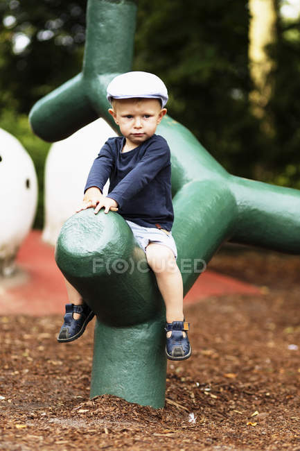 Мальчик, сидящий на зеленой конструкции на детской площадке — стоковое фото