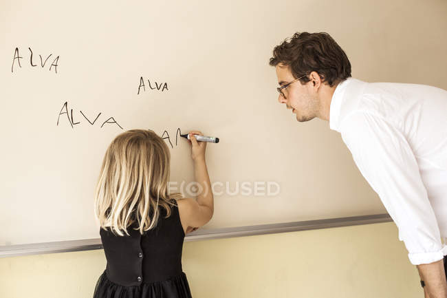 Teacher watching girl practicing writing — Stock Photo