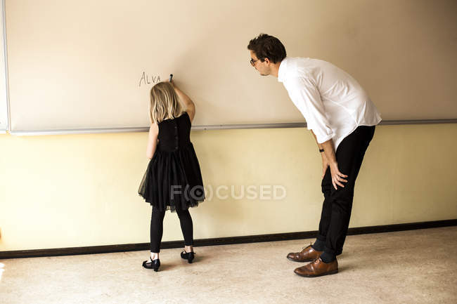 Professor assistindo menina escrevendo no quadro branco — Fotografia de Stock