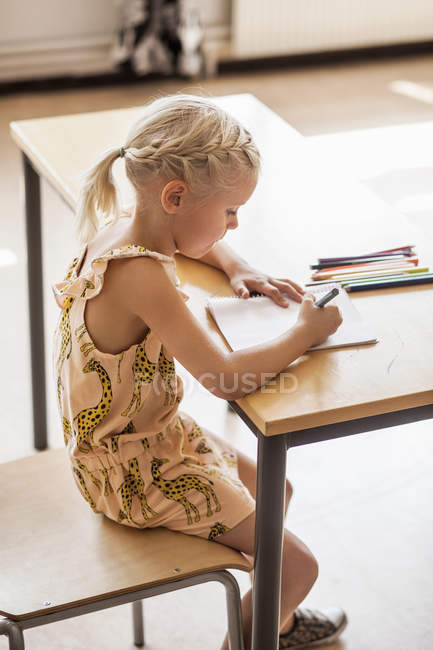 Dibujo de niña en el escritorio en el aula - foto de stock