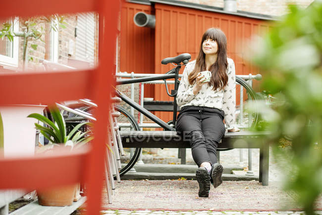 Женщина держит чашку кофе, сидя на скамейке — стоковое фото