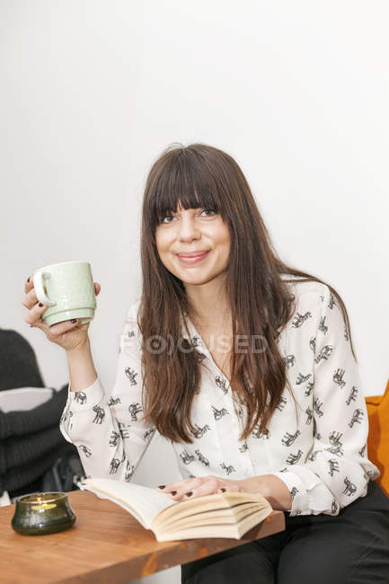 Femme avec livre tenant tasse de café — Photo de stock