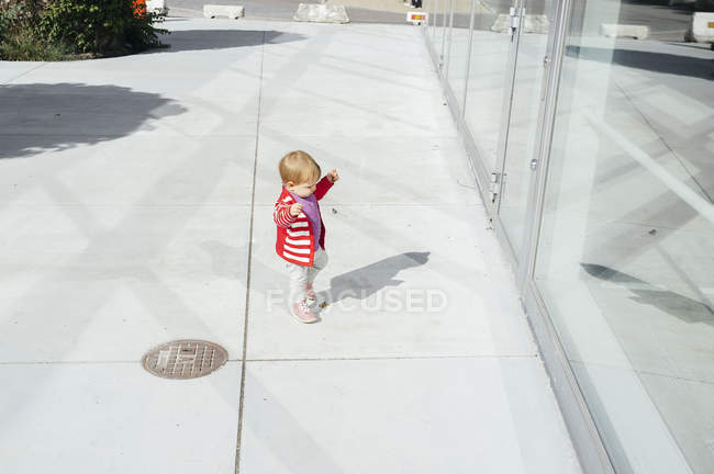 Baby girl standing outside glass building — Stock Photo