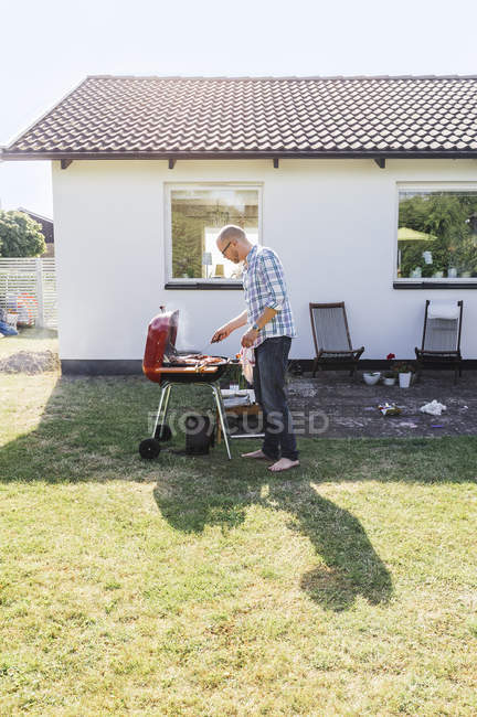 Man grilling food outside house — Stock Photo