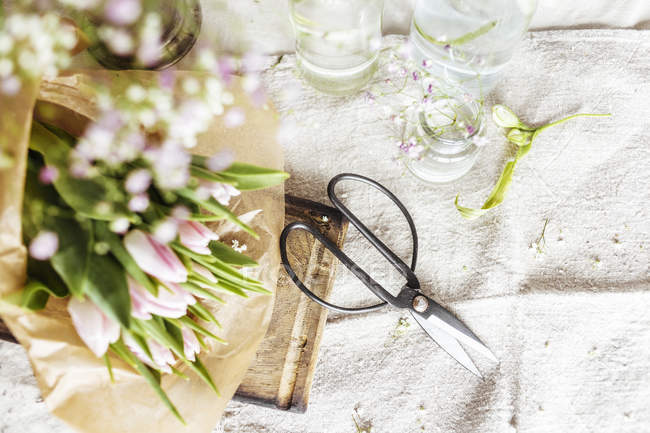 Flowers in brown paper and scissors on table — Stock Photo