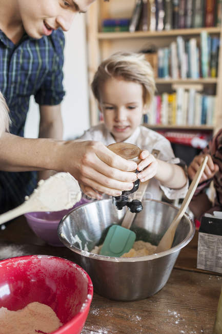 Pai e filho adicionando ingrediente na massa — Fotografia de Stock