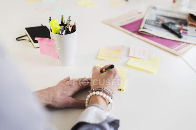 Businesswoman writing reminder at office desk — Stock Photo