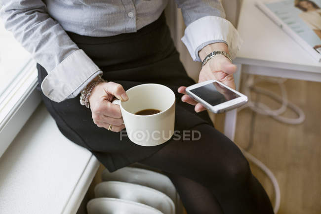 Donna d'affari in possesso di telefono cellulare e tazza di caffè — Foto stock