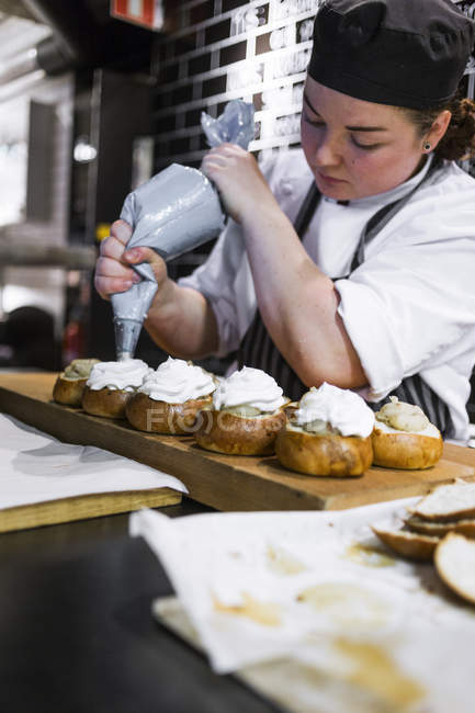 Cocinera hembra glaseado bollos en cocina - foto de stock