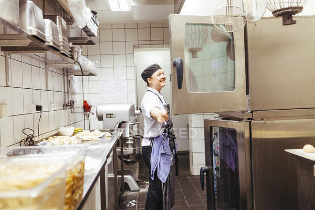 Chef mirando en el horno en la cocina comercial - foto de stock