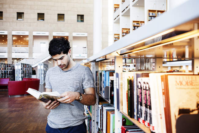 Junger Mann liest Buch in Bibliothek — Stockfoto