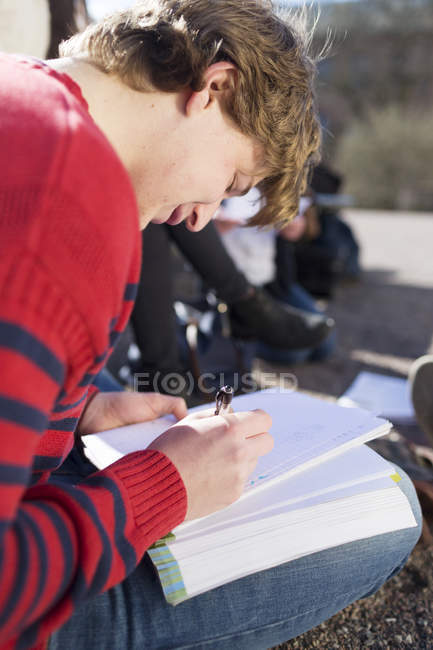 Мальчик-подросток пишет по книге — стоковое фото