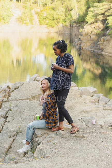 Female friends on rock by lake — Stock Photo