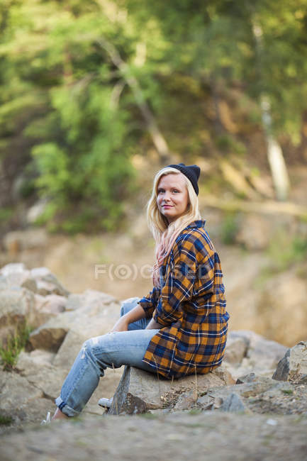 Mulher sorridente sentada na rocha na floresta — Fotografia de Stock